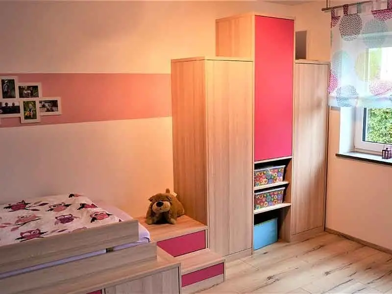 Kinderzimmer mit Bett auf Schubladenpodest, Schrank mit pinken Fächern und Regal