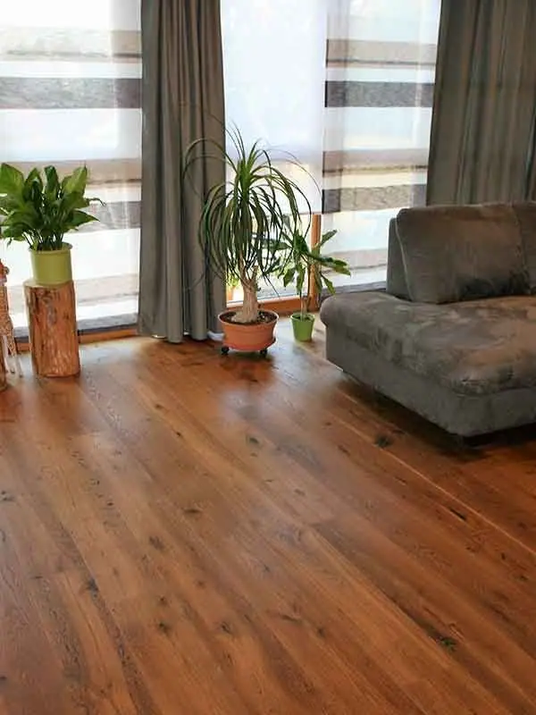 Wohnzimmer mit verlegtem Parkett, Sofa und Pflanze vor einem Fenster